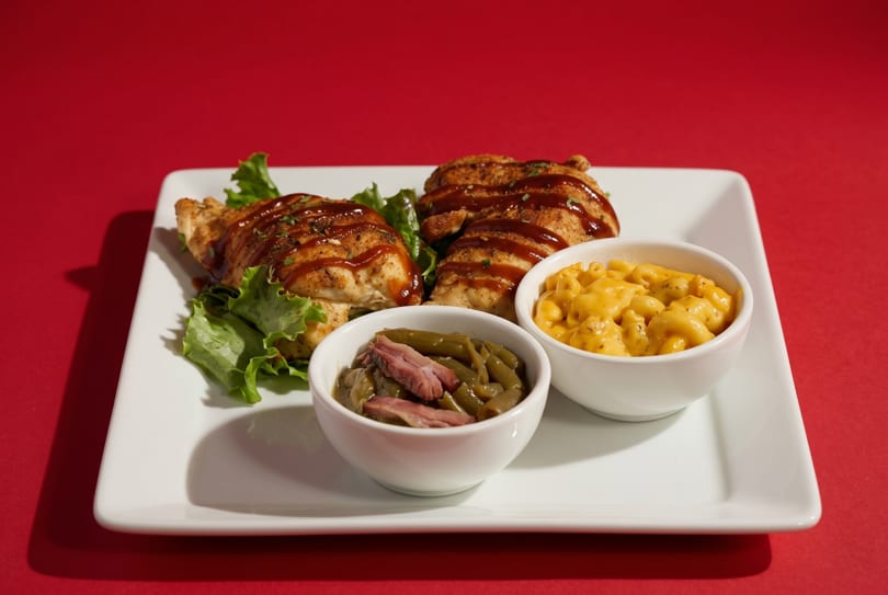 Grilled chicken with BBQ sauce, green beans, and macaroni and cheese on a white plate.