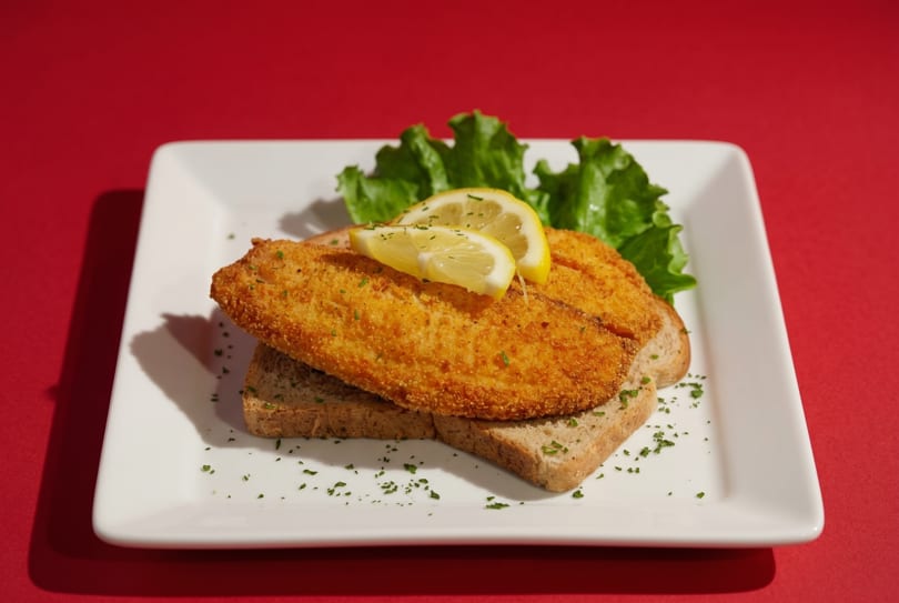 Golden-fried fish fillets on toast with lemon slices and lettuce, on a white plate.