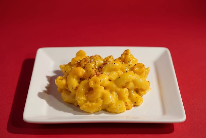 Creamy macaroni and cheese, seasoned with pepper, on a white rectangular plate against a red background.